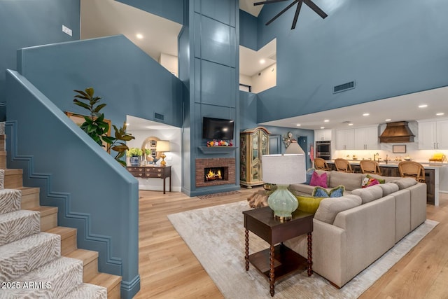 8219 S Pecan Grove Cir, Tempe, AZ 85284 - living room featuring a high ceiling, light wood finished floors, stairs, a fireplace, and ceiling fan
