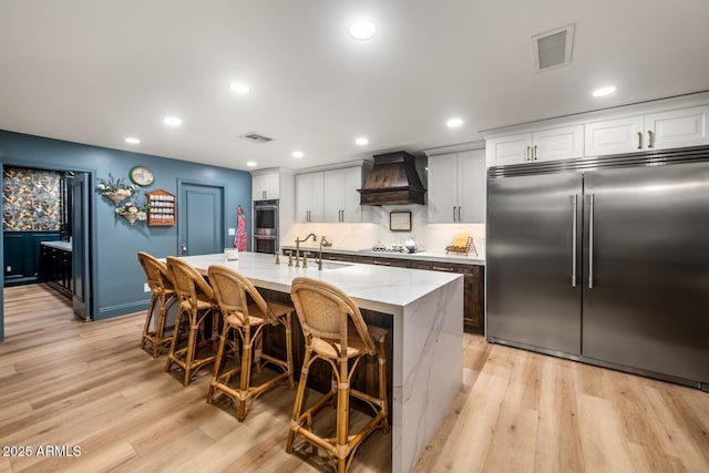 8219 S Pecan Grove Cir, Tempe, AZ 85284 - kitchen with stainless steel appliances, premium range hood, light wood finished floors, an island with sink, and recessed lighting