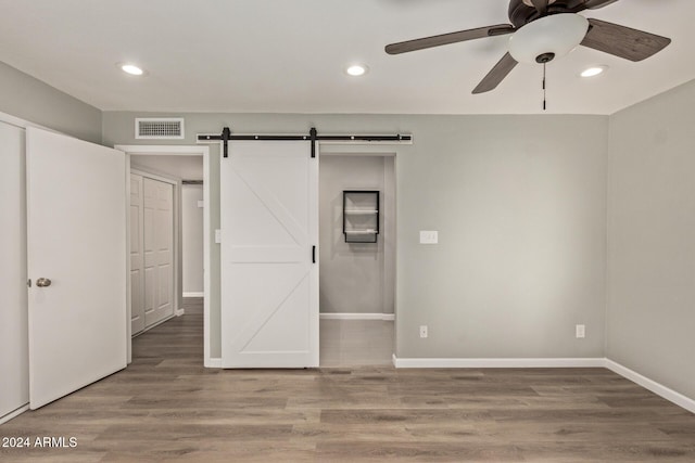 unfurnished bedroom with a barn door, wood finished floors, visible vents, and recessed lighting