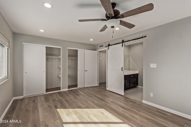 unfurnished bedroom featuring light wood finished floors, a barn door, visible vents, baseboards, and multiple closets