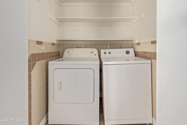 clothes washing area featuring laundry area, tile walls, and washing machine and clothes dryer