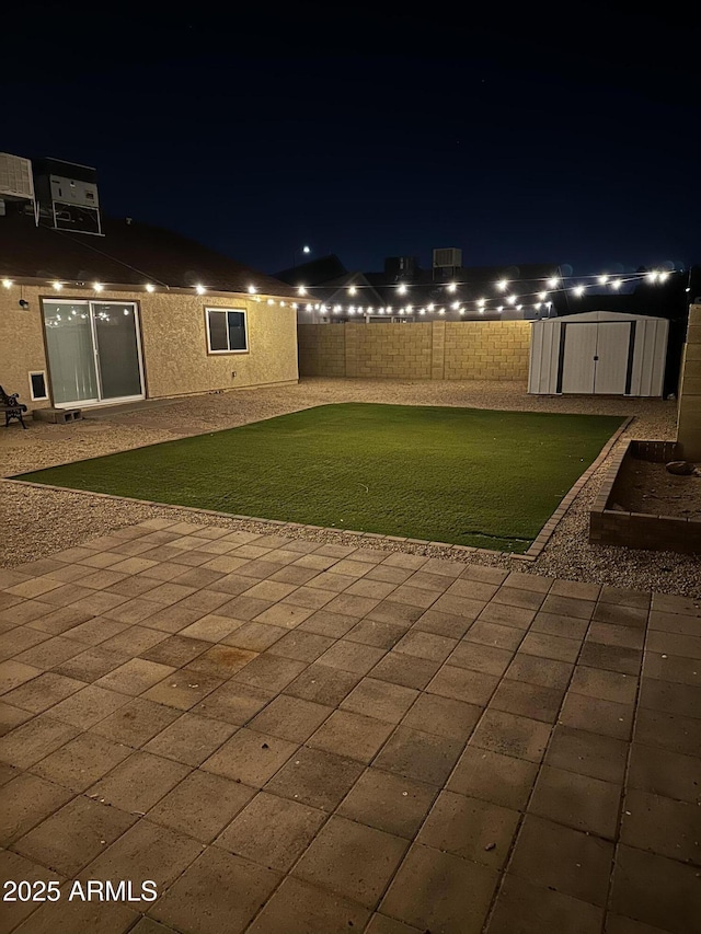 patio at twilight with fence, a storage unit, a lawn, and an outdoor structure