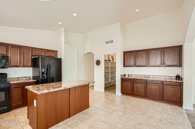 5502 N Ormondo Way, Litchfield Park, AZ 85340 - kitchen featuring black appliances, arched walkways, light tile patterned floors, a kitchen island, and a high ceiling