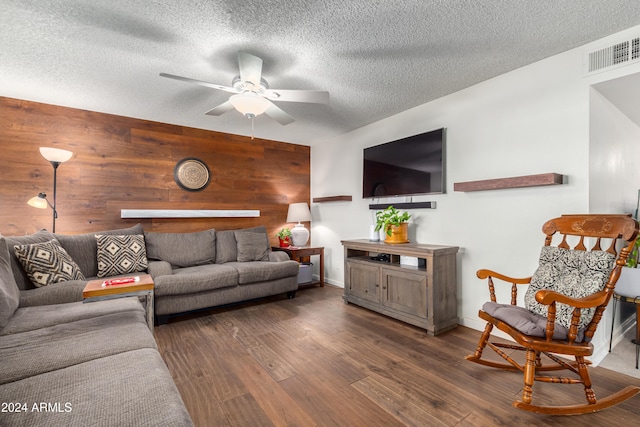 living room featuring wood walls, ceiling fan, dark wood-type flooring, and a textured ceiling