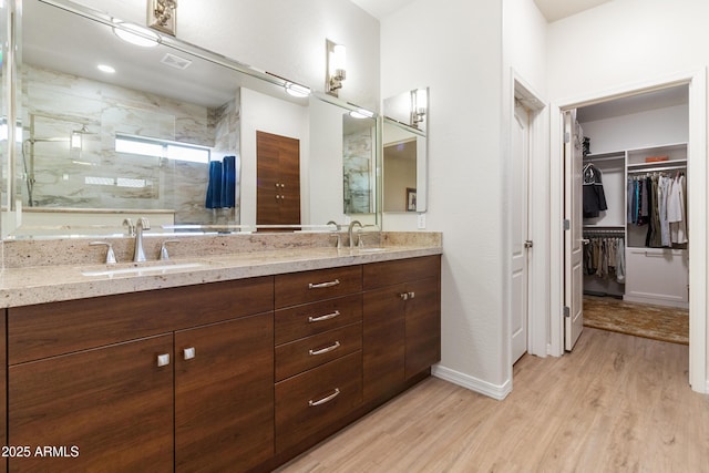 full bathroom featuring a sink, double vanity, a marble finish shower, and wood finished floors