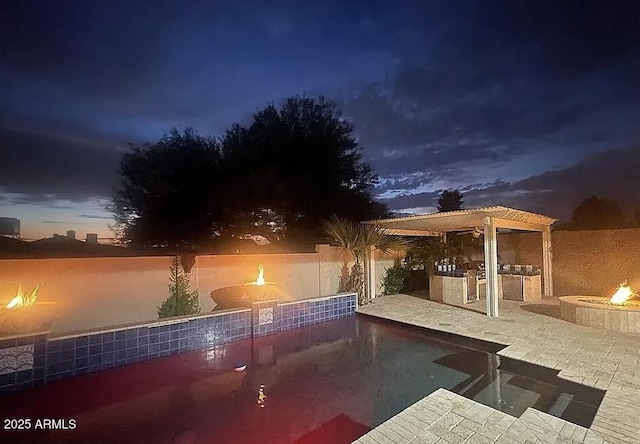 pool at twilight featuring an outdoor fire pit, an outdoor kitchen, a pergola, and a fenced backyard