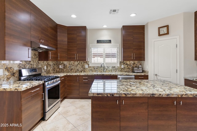 kitchen featuring light tile patterned floors, under cabinet range hood, a sink, appliances with stainless steel finishes, and decorative backsplash