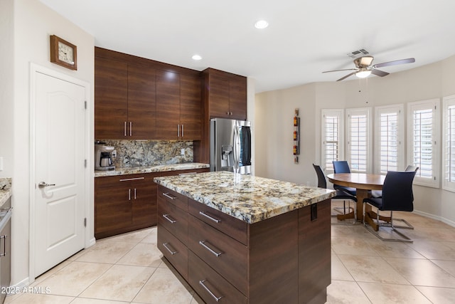 kitchen with light tile patterned flooring, visible vents, stainless steel fridge with ice dispenser, a center island, and tasteful backsplash