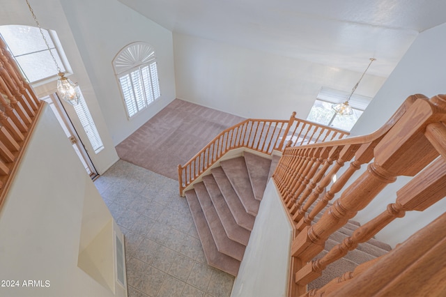 staircase with high vaulted ceiling, a chandelier, and tile patterned floors