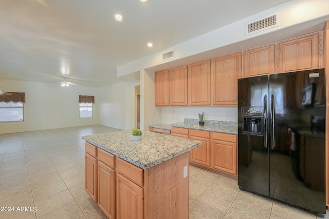 kitchen with light stone counters, a kitchen island, ceiling fan, and black fridge