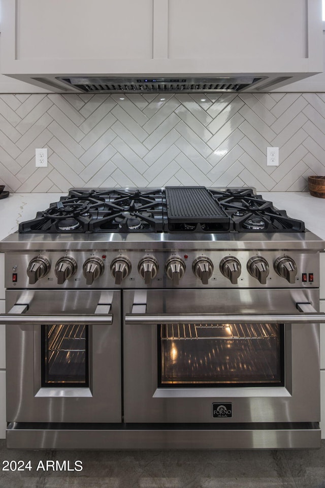 interior details featuring tasteful backsplash, double oven range, light stone counters, and white cabinets