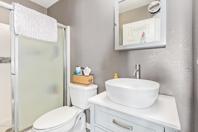 full bathroom featuring vanity, toilet, a textured wall, and a stall shower