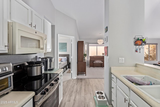 kitchen featuring white microwave, stainless steel range with electric stovetop, white cabinetry, lofted ceiling, and light wood-type flooring