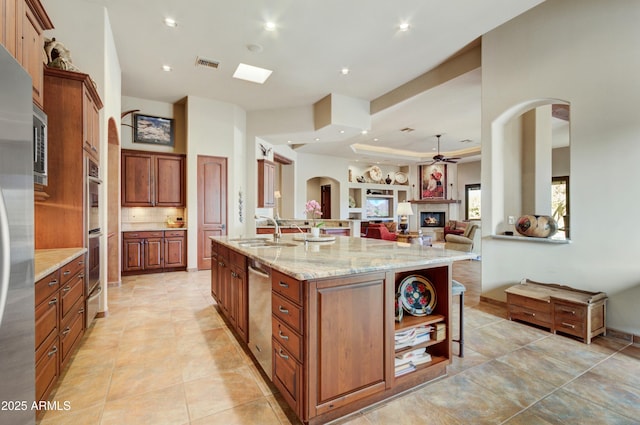 kitchen with sink, ceiling fan, light stone counters, light tile patterned flooring, and a large island with sink