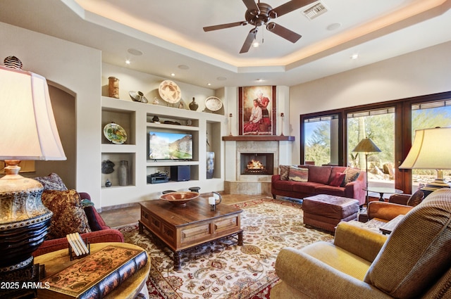 living room featuring a tray ceiling, a high end fireplace, built in features, and ceiling fan