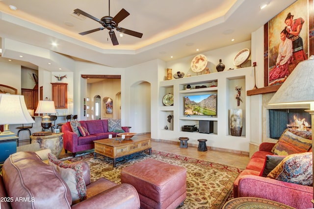 living room featuring a raised ceiling, light tile patterned floors, ceiling fan, and built in shelves