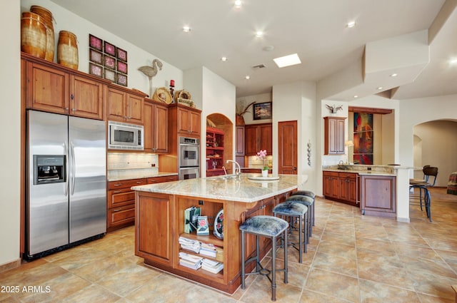 kitchen with appliances with stainless steel finishes, a center island with sink, light stone counters, tasteful backsplash, and a kitchen bar