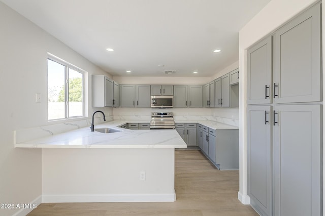 12813 W Paradise Dr, El Mirage, AZ 85335 - kitchen with stainless steel appliances, gray cabinets, a peninsula, light stone countertops, and light wood-style floors