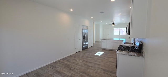 kitchen with stainless steel appliances, light stone counters, hardwood / wood-style floors, ceiling fan, and white cabinetry