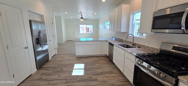 kitchen with stainless steel appliances, kitchen peninsula, light stone countertops, white cabinets, and light wood-type flooring