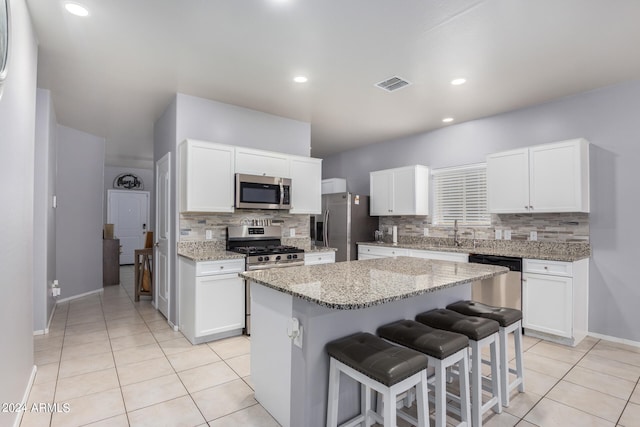 kitchen featuring backsplash, light tile flooring, stainless steel appliances, white cabinets, and a kitchen island