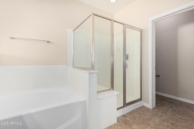 bathroom with a stall shower, a garden tub, and baseboards