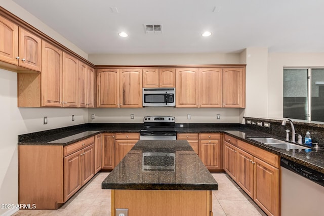 kitchen with a center island, stainless steel appliances, light tile patterned flooring, a sink, and dark stone countertops