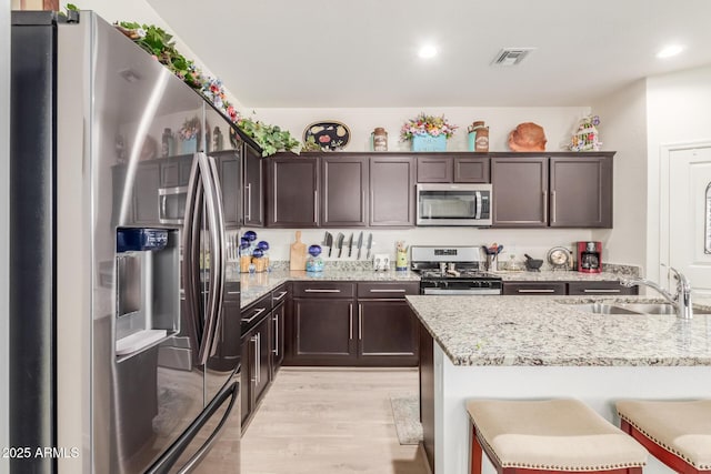 kitchen with sink, stainless steel appliances, light hardwood / wood-style flooring, a breakfast bar area, and dark brown cabinets