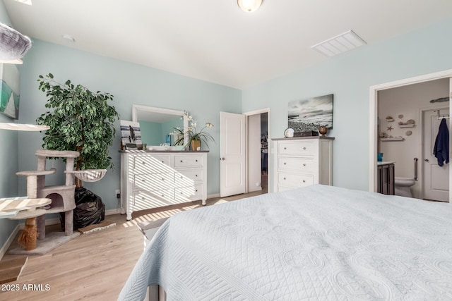 bedroom featuring visible vents, ensuite bath, baseboards, and wood finished floors