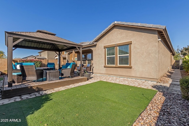 rear view of house with stucco siding, fence, a gazebo, a wooden deck, and an outdoor hangout area