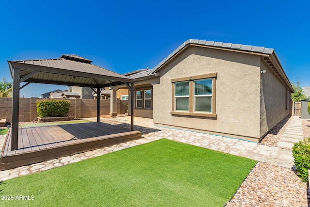 rear view of house with stucco siding, a lawn, a deck, a fenced backyard, and a gazebo