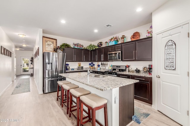 kitchen with visible vents, a breakfast bar, an island with sink, a sink, and stainless steel appliances