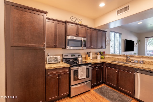 kitchen with light stone counters, sink, appliances with stainless steel finishes, and light hardwood / wood-style flooring