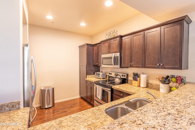 kitchen featuring light stone counters, dark brown cabinetry, sink, and appliances with stainless steel finishes