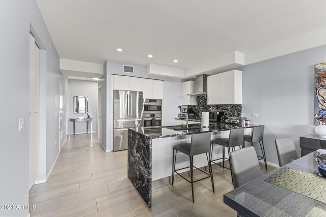 kitchen featuring white cabinetry, wall chimney exhaust hood, stainless steel appliances, kitchen peninsula, and a breakfast bar area