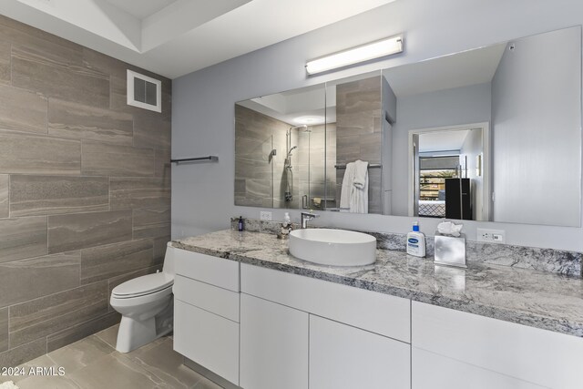 bathroom featuring toilet, vanity, tile walls, and tiled shower