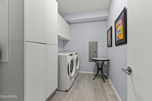 clothes washing area featuring electric panel, washer and dryer, and cabinets