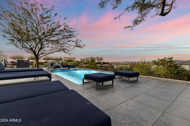 pool at dusk featuring pool water feature and a patio