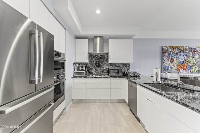 kitchen featuring dark stone counters, sink, wall chimney exhaust hood, appliances with stainless steel finishes, and white cabinetry