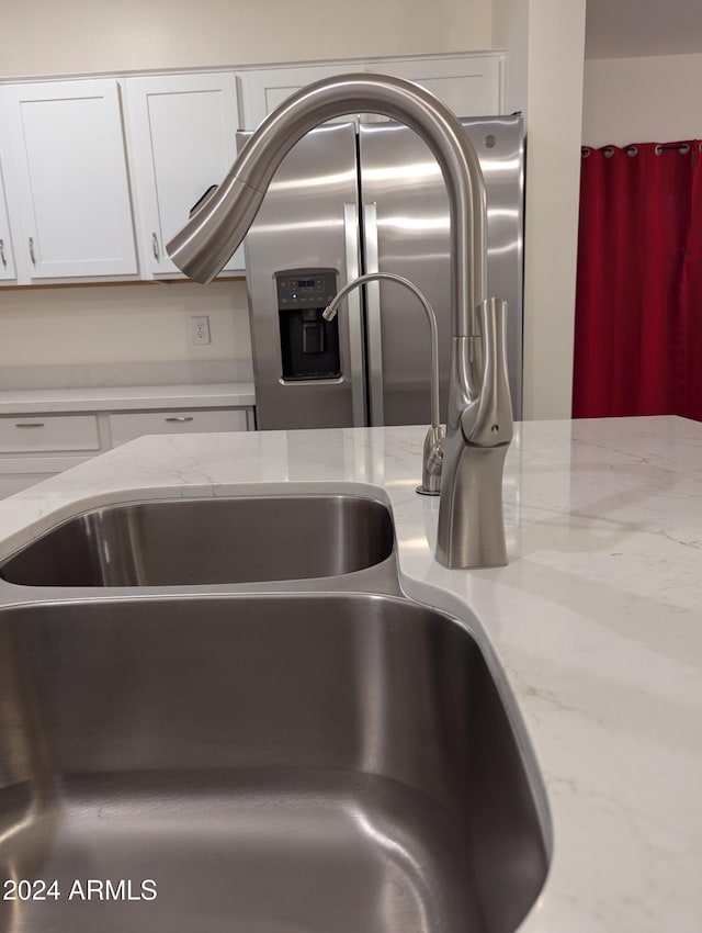 interior details with white cabinetry, light stone counters, and sink