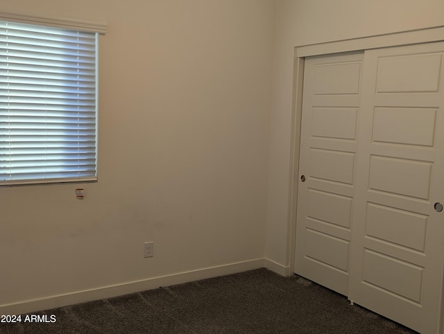 unfurnished bedroom with a closet, multiple windows, and dark carpet