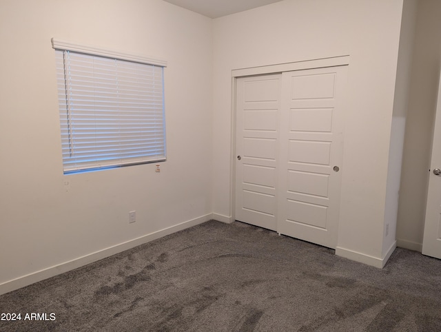 unfurnished bedroom with dark colored carpet and a closet