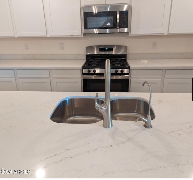 kitchen with appliances with stainless steel finishes, white cabinetry, and light stone counters