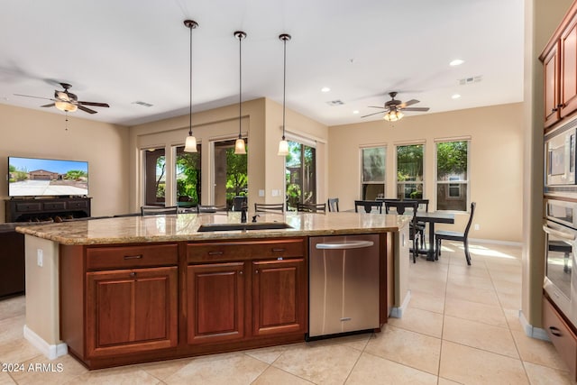 kitchen featuring light stone countertops, ceiling fan, sink, hanging light fixtures, and a center island with sink