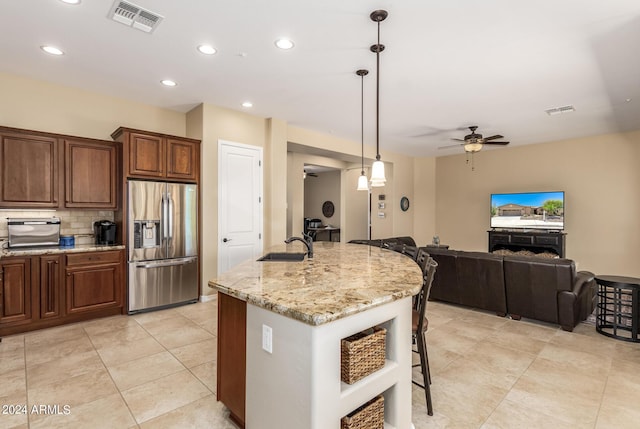 kitchen featuring a center island with sink, stainless steel refrigerator with ice dispenser, hanging light fixtures, ceiling fan, and a kitchen bar