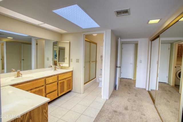 bathroom with a shower with door, tile patterned flooring, a skylight, vanity, and toilet