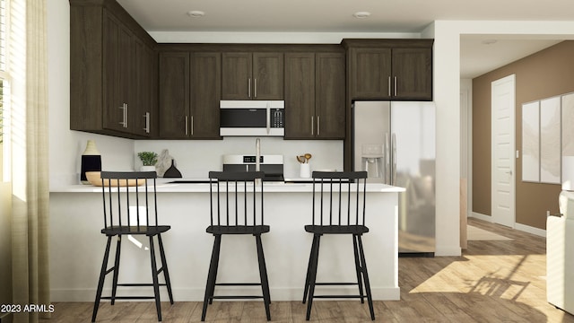 kitchen with light wood-type flooring, dark brown cabinetry, a breakfast bar area, and stainless steel fridge with ice dispenser