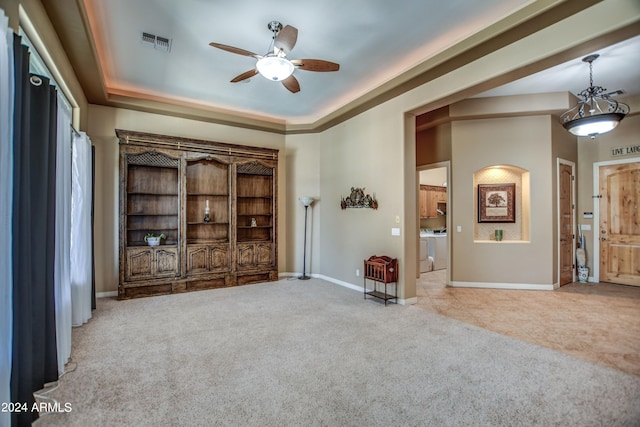 carpeted spare room with visible vents, washer and clothes dryer, a tray ceiling, baseboards, and ceiling fan