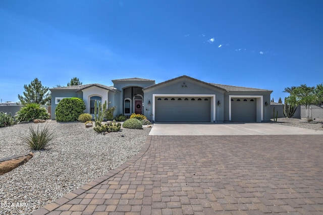 view of front of house with decorative driveway, an attached garage, fence, and stucco siding