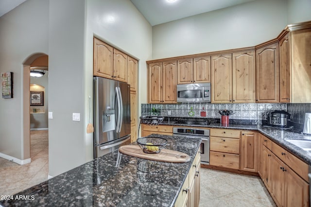 kitchen featuring dark stone counters, decorative backsplash, a high ceiling, arched walkways, and stainless steel appliances